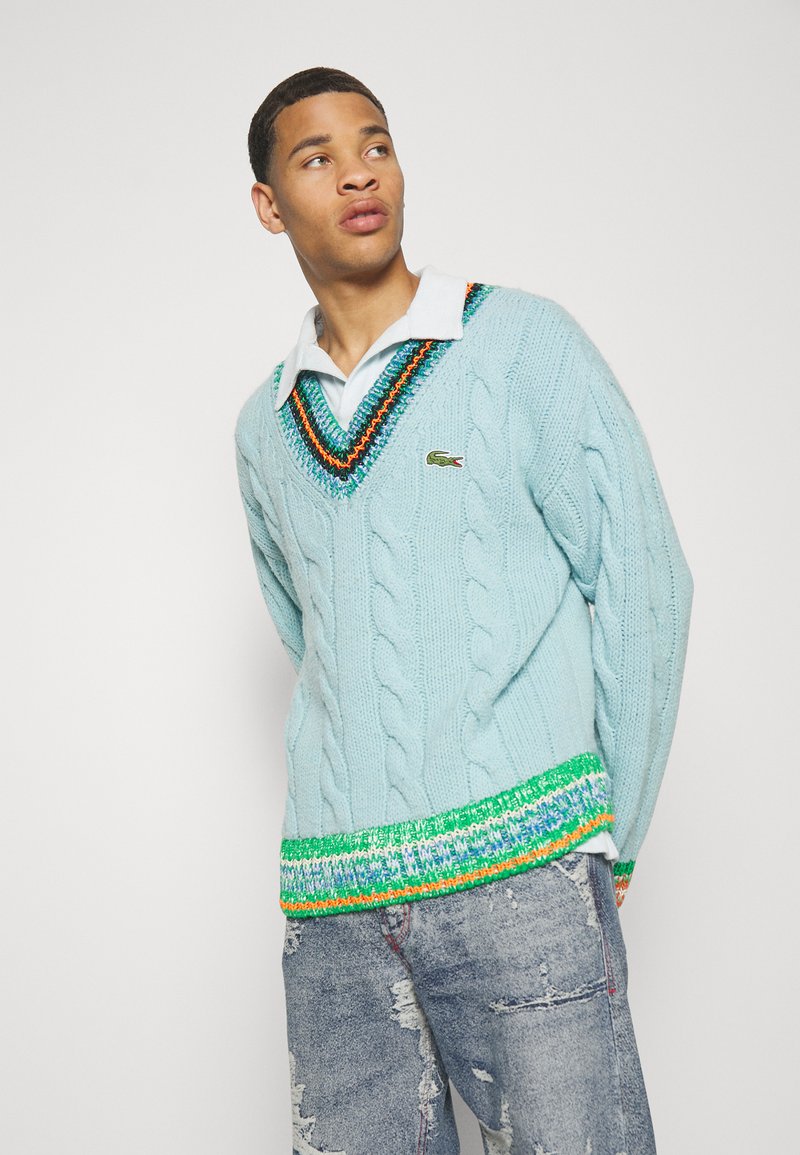 Maglione azzurro chiaro a maglia con scollatura a V profonda, con bordo a fantasia multicolore sull'orlo, abbinato a jeans in denim strappati.