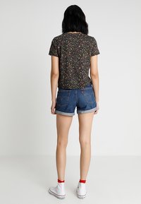 Top negro de manga corta con un patrón floral multicolor, combinado con pantalones cortos de mezclilla de talle alto y zapatillas blancas con acentos rojos.