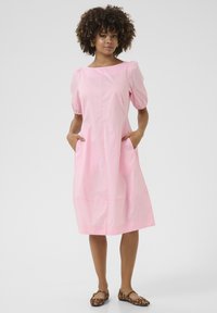 Roza, obleka srednje dolžine s puhovimi rokavi, stranskimi žepi in ravnim krojem. Nošena z balerinkami s leopardjim vzorcem. Gladek teksturiran material.