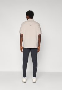 Lys beige kortermet skjorte med detalj på baksiden, sammen med mørk marine tapered bukser og hvite sneakers. Minimalistisk design.