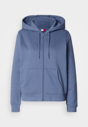 Zip-up hoodie tillverkad av mjukt, ljusblått tyg. Har en huva, två framfickor och ribbade ärmslut och nederkant. Litet logo på bröstet.