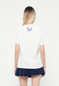 White cotton t-shirt with a round neckline, short sleeves, and a purple graphic of a face on the back. Paired with a navy pleated skirt.