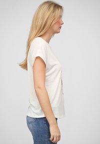 T-shirt en coton blanc avec une coupe décontractée, des manches à capuche et un imprimé graphique à l'avant. Assorti avec un jean bleu.