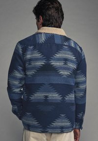 Navy blue patterned jacket with a soft beige collar, featuring geometric designs in light blue and gray tones, made from textured fabric.