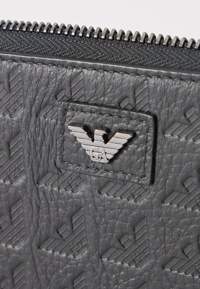 Tissu en cuir noir texturé avec des logos d'aigle embossés en répétition et un emblème d'aigle argenté cousu près d'une fermeture éclair.