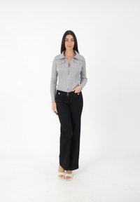 Suéter gris de canalé con cremallera y cuello, que cuenta con dos bolsillos delanteros y botones dorados, combinado con pantalones de pierna ancha negros y sandalias blancas.