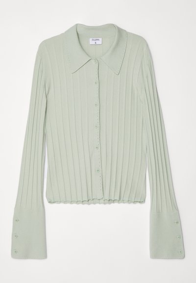 Cardigan de malha canelada verde-claro com colarinho, fecho de botão e mangas largas. Apresenta seis botões em cada manga e uma bainha com acabamento em ondas.