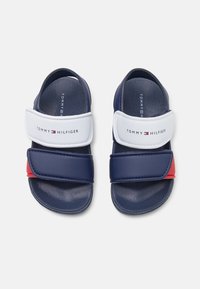 Granatowe klapki z białym paskiem i czerwonym akcentem, z teksturowaną wkładką oraz regulowanymi zapięciami na rzep.