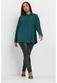 Camicia verde acqua con maniche lunghe, con dettagli luccicanti ai polsini; abbinata a leggings in ecopelle nera e sandali con tacco.