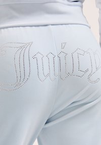 Helle blaue Hosen mit Strassverzierungen, die "Juicy" über den hinteren Taillenbund schreiben, getragen mit einem passenden hellblauen Oberteil.