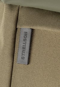 Olive zelena teksturirana tkanina z vdelanim šivom; vsebuje pravokotno črno etiketo z vtisnjenim napisom "STRELSON" za blagovno znamko.