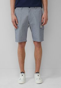 Pantaloni cargo a righe bianche e blu con tasche laterali, realizzati in un tessuto leggero. Indossati con scarpe da ginnastica bianche con dettagli blu navy.