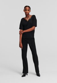 Top negru cu maneci scurte, cu un guler asimetric, asortat cu pantaloni negri croit și cu toc înalt, ascuțit, negri. Accesoriu: colier din lanț argintiu.
