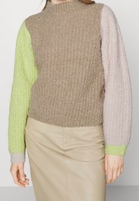 Pull en maille à col montant, avec un corps marron, des manches vertes, rose pâle et gris clair, et une texture côtelée sur l'ensemble.