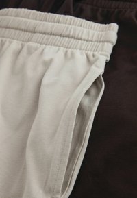 Nadrág elasztikus derékpánttal, egyik oldala világos bézs pamutból, a másik sötétbarna, sima tapintású, mintázat nélküli.