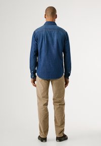 Donkerblauwe denim overhemd met lange mouwen en knoopmanchetten, gecombineerd met lichtbeige corduroy broek. Gladde textuur en een getailleerde pasvorm.