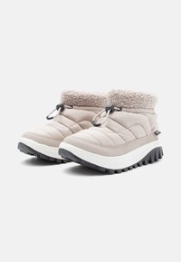 Beige quiltede vinterstøvler med en lodden krage, sort gummisål og snøring. Har en polstret overdel og teksturert såle.