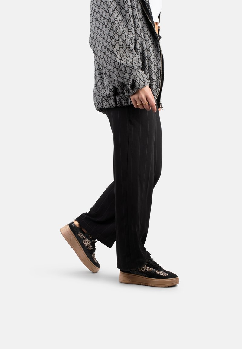 Doudoune à motif noir et blanc, pantalon large noir à rayures, et baskets noires avec accents floraux et semelles beiges.