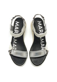 Sandalias grises con varias texturas, incluyendo correas brillantes y mate, correas de tobillo ajustables y una suela plana. Plantilla negra con marca.