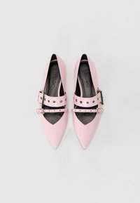 Růžové lakované boty s špičatou špičkou a dvojitými pásky se stříbrnými hroty. Uvnitř mají černé podšívku s logem "HUGO".