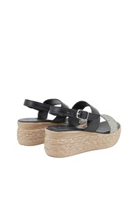 Sandali in pelle nera con cinturino scintillante, fibbia regolabile e suola piattaforma in juta intrecciata. Presentano una finitura testurizzata e naturale.