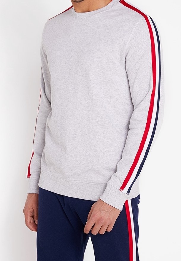 Sudadera gris de manga larga con rayas rojas y azul marino a lo largo de las mangas. Tejido suave con cuello redondo y puños acanalados.