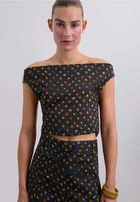 Top negro con hombros al descubierto que presenta un patrón geométrico en naranja, verde y amarillo; diseño corto con una textura suave.
