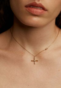 Collar de cadena de oro con un pequeño colgante en forma de cruz que presenta una gema central. Superficie lisa y pulida con diseño de cadena enlazada.