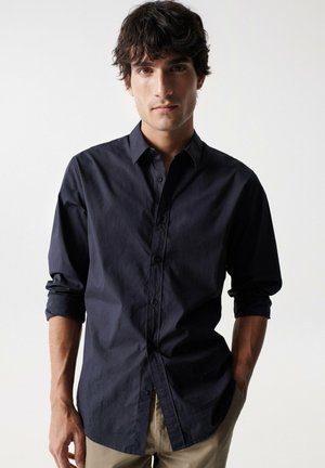 Camisa de botón de manga larga de color azul marino con un cuello rígido, tejido texturizado y un corte ajustado, combinada con pantalones caqui.