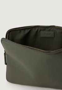 Zielona oliwkowa torba na zamek wykonana z gładkiego materiału, charakteryzująca się zorganizowanym wzornictwem oraz wewnętrzną etykietą oznaczoną jako "ZIGN." Wewnętrzna tekstura jest matowa.