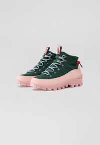 Zapatillas de plataforma altas de punto en verde con suela gruesa rosa, que presentan cordones grises, ojales negros redondos y detalles rojos en el talón.