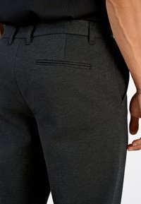 Tumedat halli tekstuurse kangaga püksid, mis on varustatud ühe tagatasku ja sujuva vöökohaga.