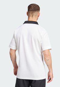 Hvid poloshirt med en sort krave. Korte ærmer, glat tekstur og afslappet pasform. Synlig tatovering på underarmen. Enkelt design.