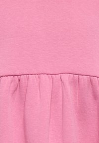 Ανοιχτό ροζ βαμβακερό ύφασμα με λεπτομέρειες ρυτίδωσης στο τελείωμα, δημιουργώντας υφή με βολάν. Λείο ύφασμα και ομοιόμορφη ραφή.