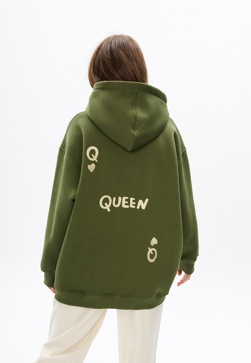 Felpa oversize verde oliva con scritte color crema che dicono "Q QUEEN" e disegni di cuori. Il tessuto appare morbido con una texture liscia.