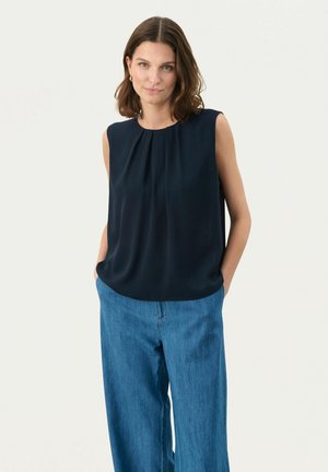Blusa senza maniche blu navy con dettagli plissettati sul collo, abbinata a pantaloni larghi in denim chiaro. Tessuto dalla consistenza liscia.