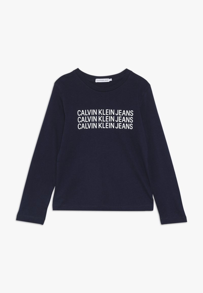 T-paita, jossa pitkä hiha, tummansinistä puuvillaa, jossa "CALVIN KLEIN JEANS" -logo painettuna valkoisena. Klassinen pyöreä pääntie ja rento istuvuus.