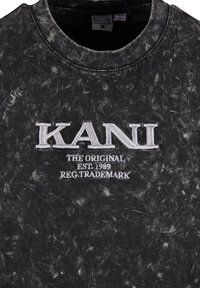Fekete, vintage stílusú pulóver, elhalványult textúrával. Kiemelkedő fehér hímzett "KANI" logóval és szöveggel rendelkezik, beleértve a "THE ORIGINAL EST. 1989." feliratot.