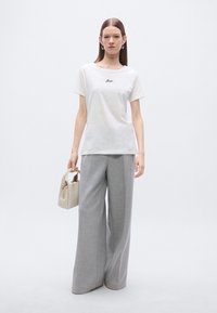 Λευκό βαμβακερό t-shirt με κοντά μανίκια, κεντημένο κείμενο στο στήθος, συνδυασμένο με ανοιχτό γκρι παντελόνι φαρδιάς γραμμής και μικρή μπεζ τσάντα χειρός.