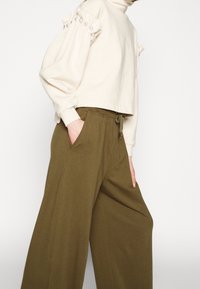 Beige kortärmad tröja med puffärmar och pärldetaljer, kombinerad med olivgröna vida byxor med framfickor och dragsko i midjan.