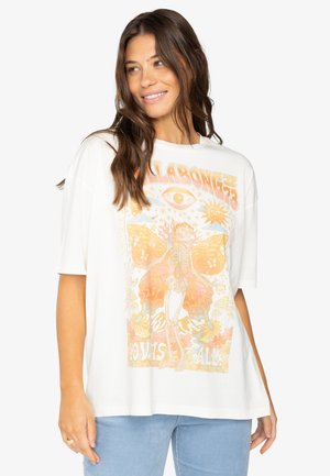 Camiseta blanca de gran tamaño con un colorido estampado gráfico de un esqueleto con alas de mariposa, acentos florales y texto de inspiración retro.