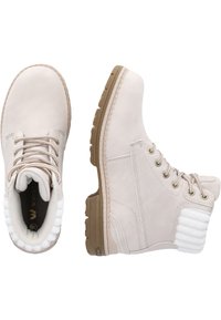 Botas de tobillo de color beige claro con un acento de piel sintética blanca texturizada, punta redonda, ojales de metal y una suela de goma con un dibujo en el patrón.