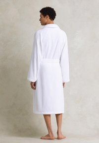 Accappatoio bianco in spugna con colletto a scialle, maniche lunghe e cintura da annodare. Presenta una vestibilità comoda e un design fino al ginocchio.