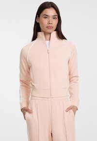 Lichtroze zip-up sportjack met witte accenten, hoge kraag, geribbelde manchetten en een aansluitend ontwerp, gecombineerd met bijpassende lichtroze broek.