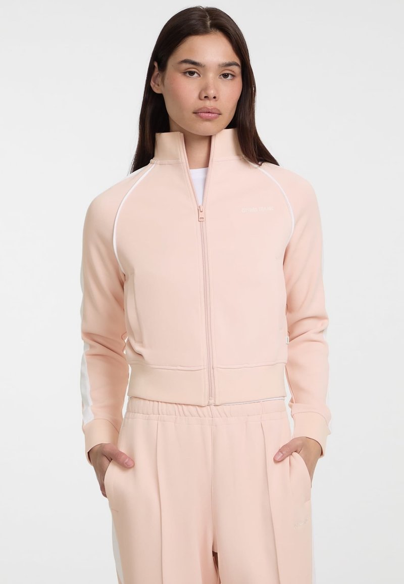 Lichtroze zip-up sportjack met witte accenten, hoge kraag, geribbelde manchetten en een aansluitend ontwerp, gecombineerd met bijpassende lichtroze broek.