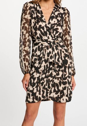 Vrouw draagt een lange mouw, V-hals wikkeljurk met een zwart-beige abstracte dierenprint en een gestrikte taille riem.