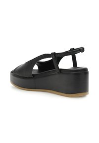Svarta plattformssandaler med en texturerad läderöverdel, öppna sidor och en slät gummisula med en svag kurva. Minimala metallaccenter.