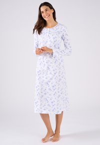 Camisa de noche de manga larga en algodón blanco con un estampado floral azul, escote redondo y detalles de botones. El dobladillo cae por debajo de la rodilla.