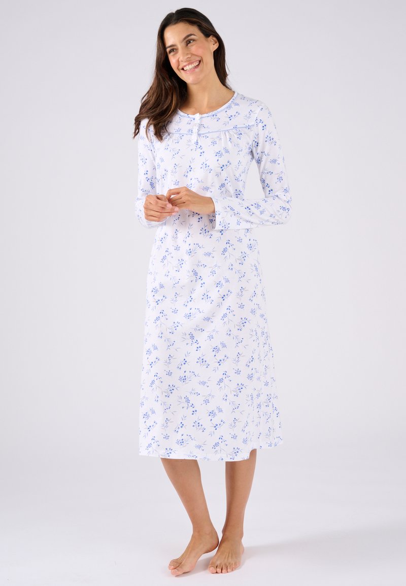 Camisa de noche de manga larga en algodón blanco con un estampado floral azul, escote redondo y detalles de botones. El dobladillo cae por debajo de la rodilla.
