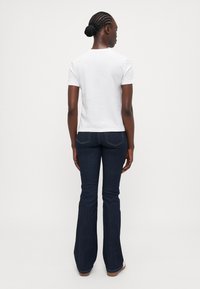White short-sleeve t-shirt with a round neckline, paired with dark blue flared jeans, showing a back view of the outfit.